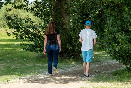 the backs of a woman and boy walking at distancing from one another through a park
