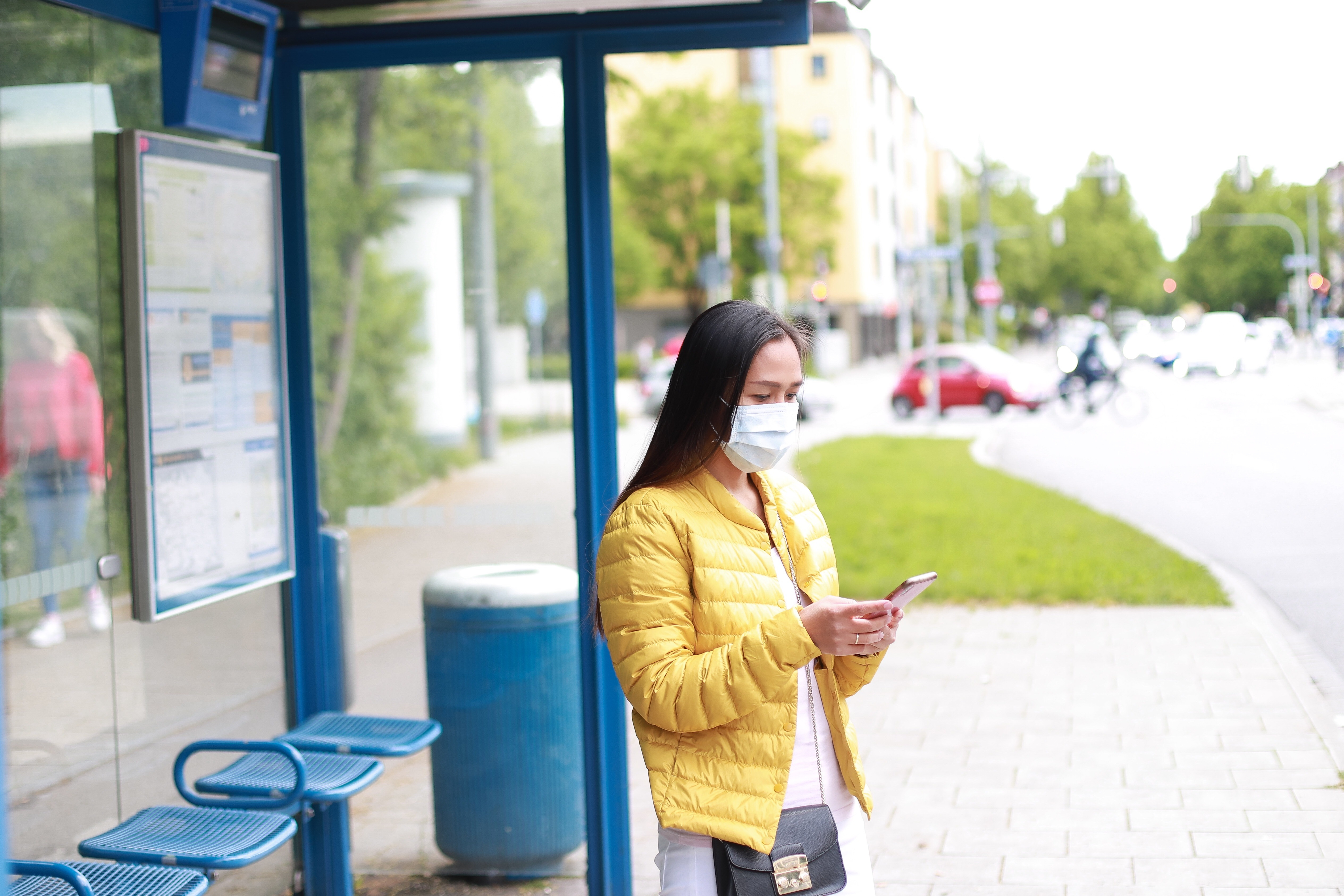 Young asian girl standing at bus stop with face mask and phone